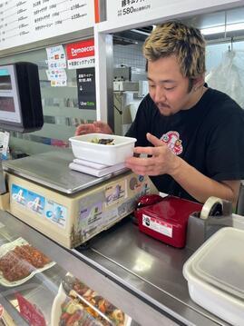 写真：持参容器にお惣菜を入れる店長